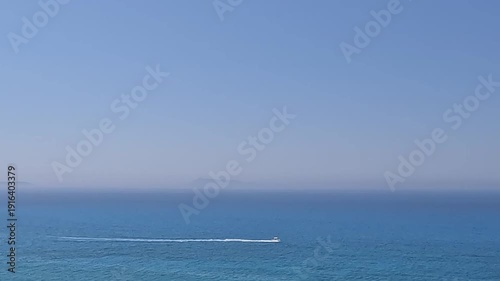 Wide view of blue sea horizon with small speedboat and hazy mountains