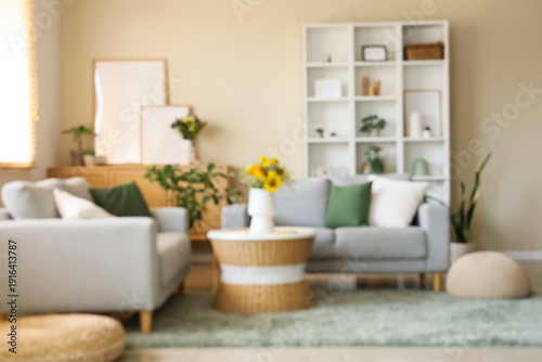 Cozy sofas and wild flowers in vase on coffee table in interior of living room. Blurred view