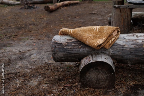 A blanket is placed on a log by a forest with fallen branches around it