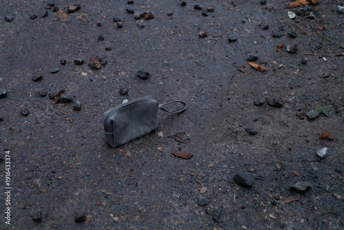 A wallet rests on a dirt ground scattered with small stones and debris in an outdoor area