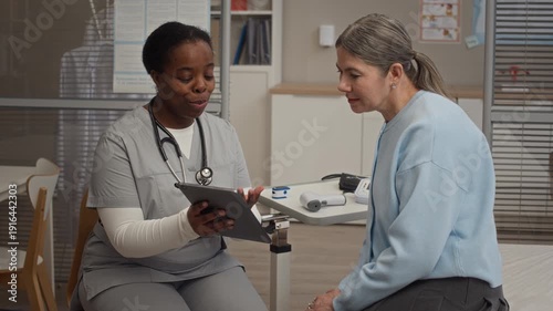 Black female healthcare professional reviewing medical test results on tablet with Caucasian female patient during consultation in modern clinic office
