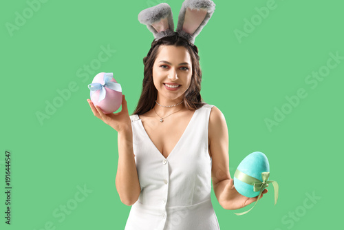 Beautiful woman in bunny ears with Easter eggs on green background