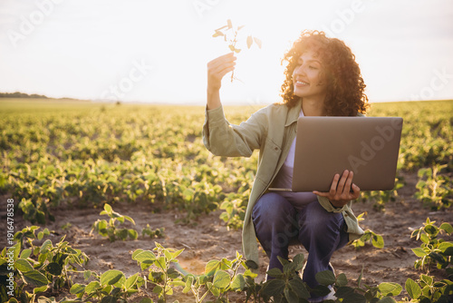 Obraz na płótnie Young agronomist holding soybean plant and laptop in cultivated field