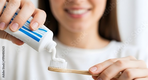 A woman applying toothpaste to a bamboo toothbrush in a clean and minimalist bathroom setting