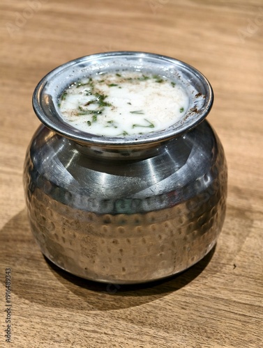 Traditional Indian buttermilk served in a hammered steel pot, garnished with herbs and spices, showcasing refreshing desi beverage presentation on a wooden table with authentic rustic appeal.