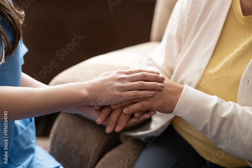 Close up young caregiver holding hands elderly patient for emotional support empathy home. Healthcare nursing service concept senior woman receiving kindness from professional assistant.