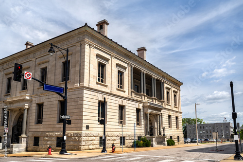 Former Kansas City Public Library building in Missouri. Historic Neoclassical architecture features massive stone blocks and ionic columns at a downtown street corner under a blue sky