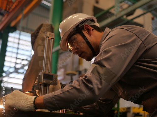 Asian engineer measuring metal automotive parts with height gauge in factory workshop