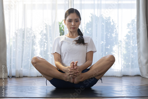 Free Download Woman practicing butterfly yoga pose indoors on mat, natural window light, healthy lifestyle, home workout, mindfulness and flexibility training concept - GFXLoad