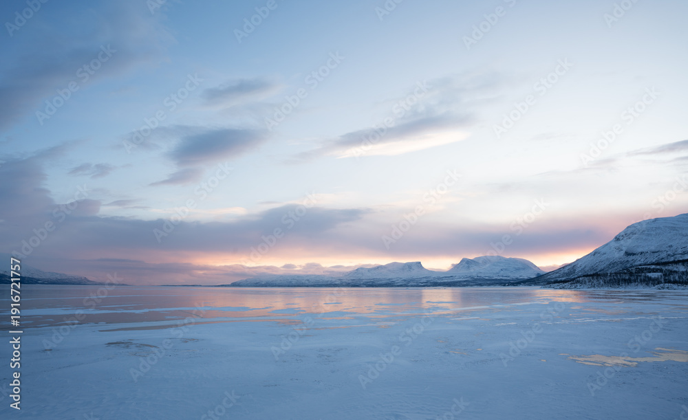 Fototapeta premium Frozen winter landscape near Abisko national park at sunrise, with Lapporten, arctic mountains, and smooth ice