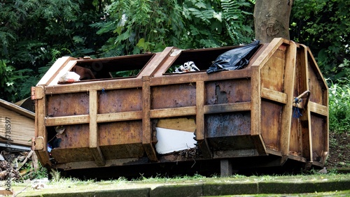 Billede på lærred Large rusted metal dumpster sitting in a park area with green trees in the background