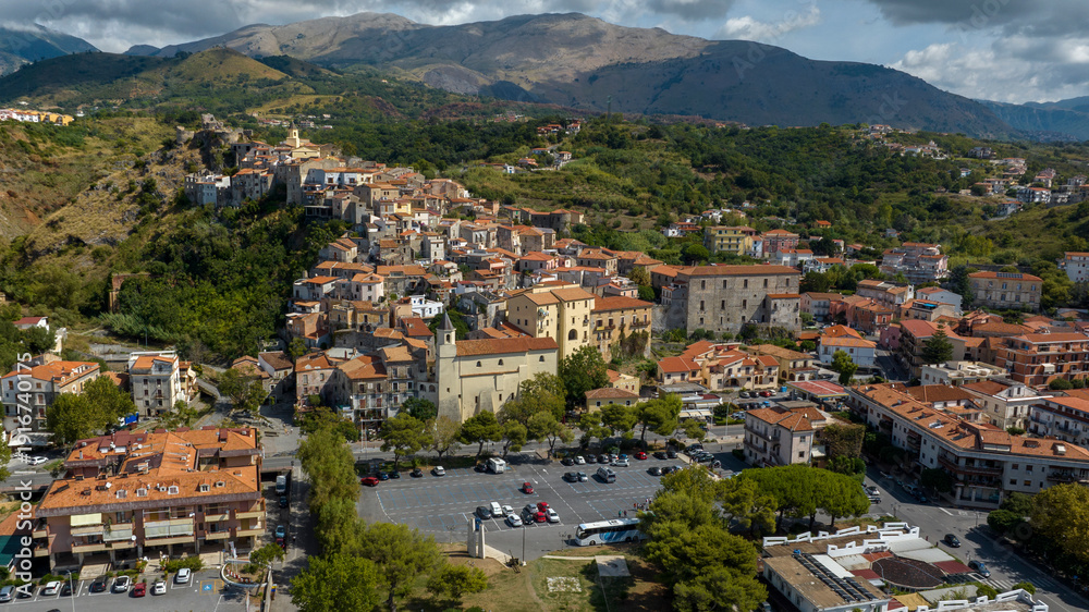Fototapeta premium Aerial view of a historic town nestled against a lush hillside. Panorama of Scalea, a town in the province of Cosenza, in Calabria, Southern Italy. The Calabrian Apennines are in the background.