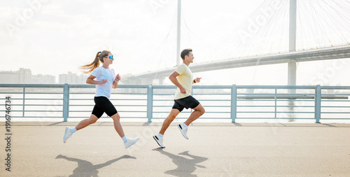 Fotografija Runners enjoy a morning jog along the waterfront near a bridge in a city