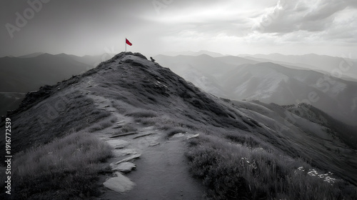 A lone vibrant red flag proudly stands on the rugged peak of a dramatic grayscale mountain, symbolizing achievement, the culmination of a challenging journey, and ultimate success