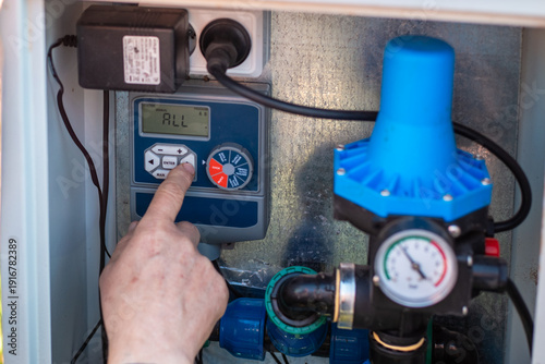 A man hand presses a button on a digital pump controller with a pressure gauge. smart irrigation, water management, garden technology.
