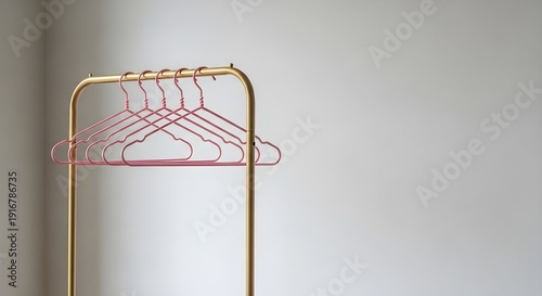 Five empty pink wire clothes hangers hanging neatly on a minimalist golden garment rack
