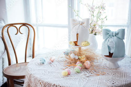 Wallpaper Mural Decorative Easter table setting featuring pastel-colored eggs, floral arrangements, and two cake stands with bows, all arranged on a lace tablecloth near a window Torontodigital.ca