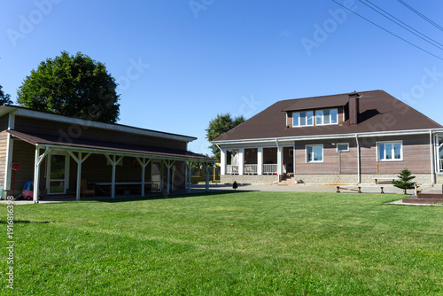 Residential house with porch lawn and wooden structures under clear blue sky. Well maintained countryside home with porch carport and wooden annex ideal for real estate architecture lifestyle.