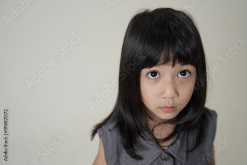 Asian little girl looking up with big eyes on neutral background, child portrait expressing curiosity and innocence.