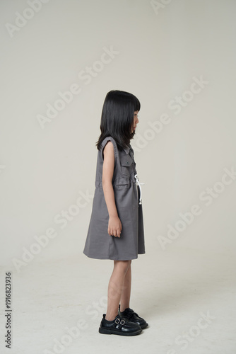Side view full body Asian girl in gray dress on neutral background, children fashion profile portrait.