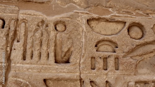 Closeup of ancient Egyptian hieroglyphic inscriptions with cartouches and bird symbols carved in sandstone wall at Medinet Habu temple in Luxor Egypt, detailed royal text.