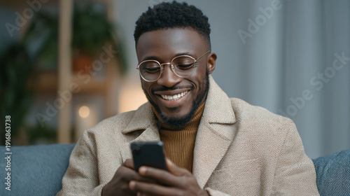 A smiling man using a smartphone indoors with a cozy background.