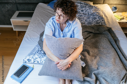 Thoughtful confident White woman hugging pillow on bed after work