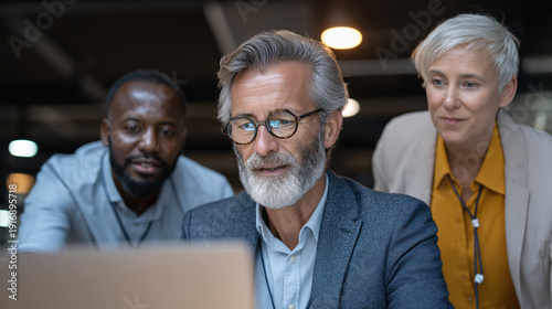 Three professionals gathered around a laptop in a modern office setting.