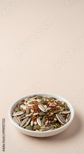 Small white dish filled with a simple mix of sunflower, flax and pumpkin seeds positioned near the bottom center of a pale beige surface, vast empty upper area acting as negative space.