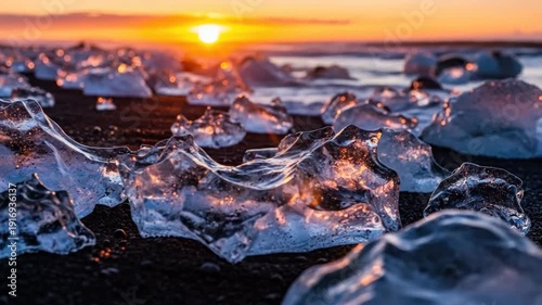 Chunks of ice are scattered on the black sand beach at sunset.