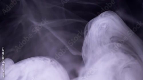 Thick plumes of white smoke curl and rise slowly against a deep black background, creating fluid patterns. Concept of mystery, magic, vape clouds, and ethereal dark atmosphere.
