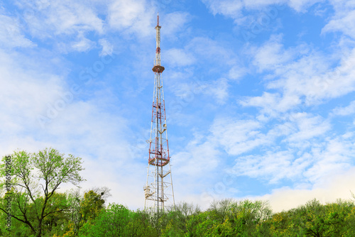 Tall telecommunication tower reaching into a bright blue sky with fluffy white clouds