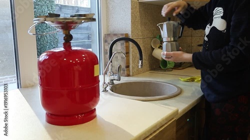 A young Ukrainian woman lights a gas stove with a match to make herself coffee during a power outage. The intimate kitchen scene highlights everyday resilience and adaptation to electricity shortages 