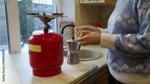 A young Ukrainian woman lights a gas stove with a match to make herself coffee during a power outage. The intimate kitchen scene highlights everyday resilience and adaptation to electricity shortages 
