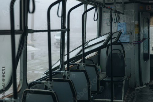 Interior of a public bus with window frames bent inward and shattered glass on the floor after an explosion. Aftermath of a missile strike or shelling on civilian transport infrastructure.