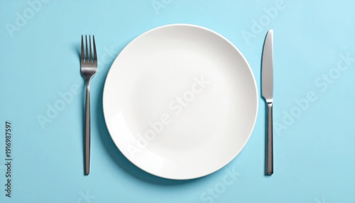 Empty white plate with fork and knife on solid light blue background view