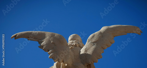 фотографія Ancient angel sculpture with outstretched wings against clear sky, evoking transcendence, faith, and eternal ascent