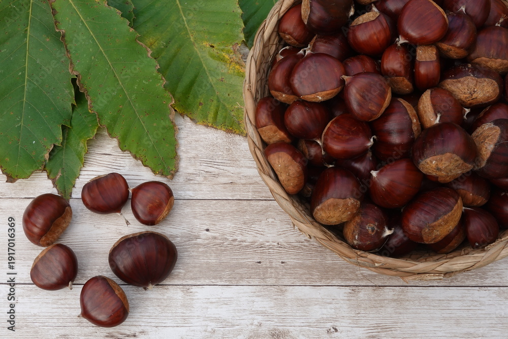 Fototapeta premium Fresh chestnuts filling wicker basket on wooden table