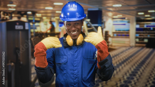 фотографія Man construction worker points both index fingers wearing blue hardhat yellow earmuffs and work gloves in studio; confidence safety readiness