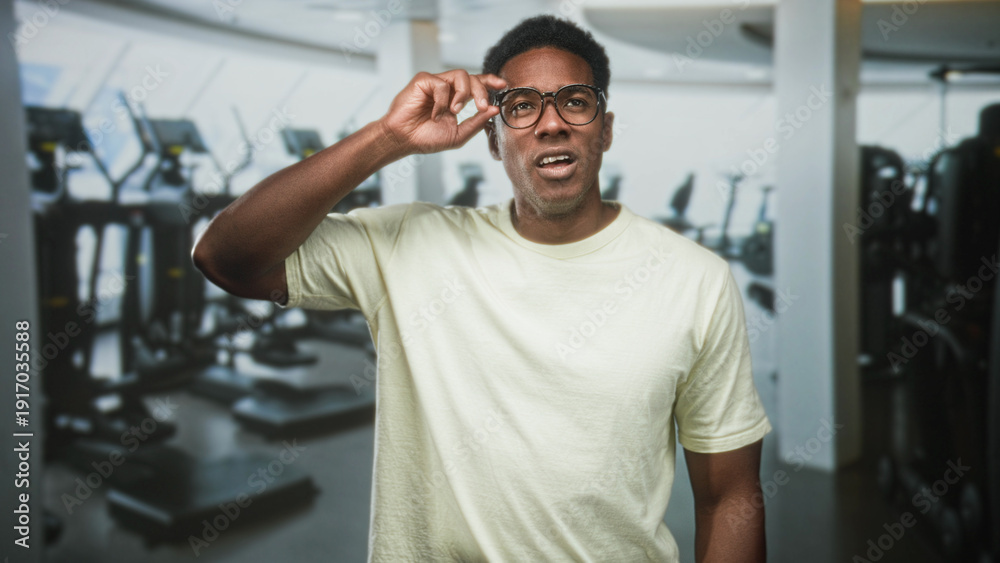 © Krakenimages.com - Man lifting glasses with right hand, squinting while inspecting gym equipment in a fitness building; confusion.