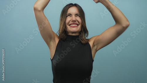 Photography Young hispanic woman pointing finger with extended arms in blue studio setting and black sleeveless top; joy confidence