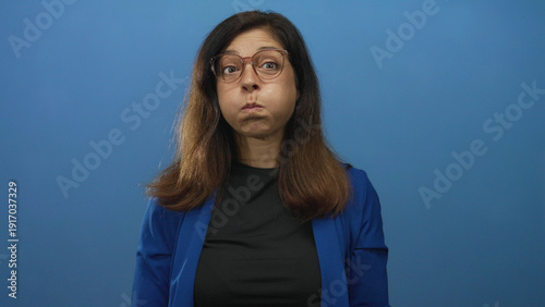 Obraz na płótnie Hispanic middle aged woman wearing glasses and pushing her cheeks with her fingers in studio; playfulness