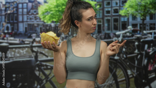 Woman pointing at a clear bowl of potato chips by a canal with a dubious look on her face; indecision choice.