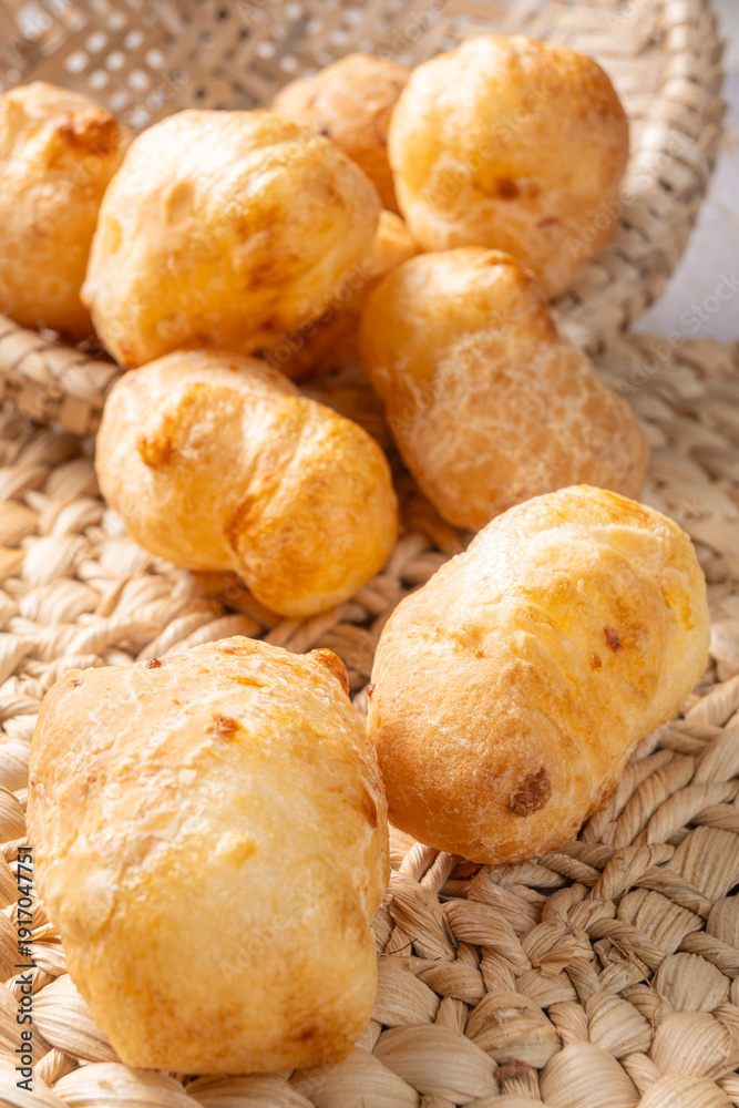 Fototapeta premium Cheese bread, a delicious Brazilian cheese bread, in a basket on a rustic woven straw surface, selective focus.