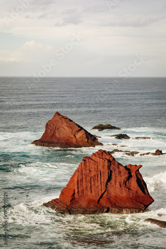 Canvastavla Rocky coastal formations rise from the ocean waves, showcasing distinct red hues