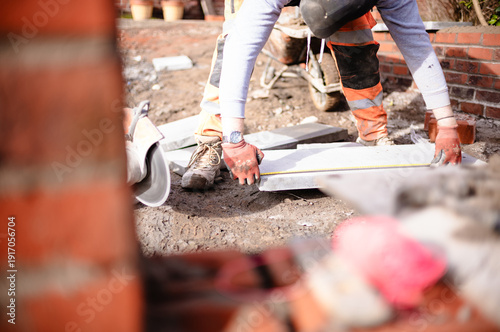 builders cutting, measuring and laying concrete block to build a wall wearing full personal protection equipment 