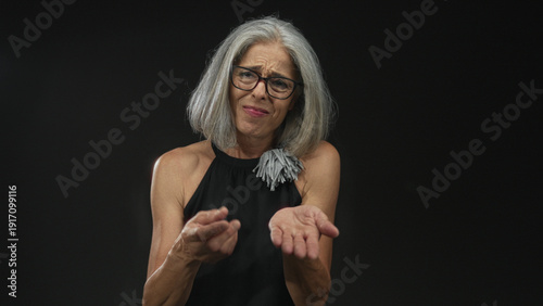 Woman with outstretched hands making pleading gesture in studio against a black wall; uncertainty asking help.