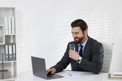 Businessman working with laptop at table near white wall indoors