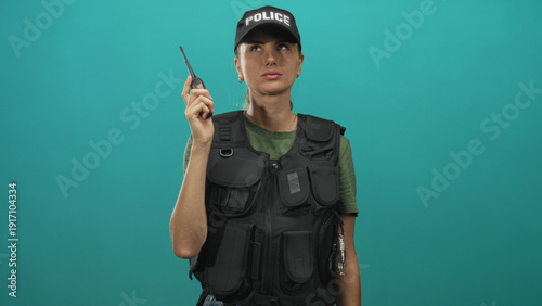 Bilde på lerret Woman police officer holds walkie talkie in right hand, wearing tactical vest and cap with police, pouting and shrugging in studio; frustration