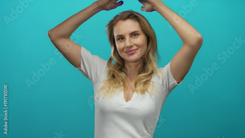 Woman gesturing with hands overhead against green background showcasing smiling expression and blonde hair.